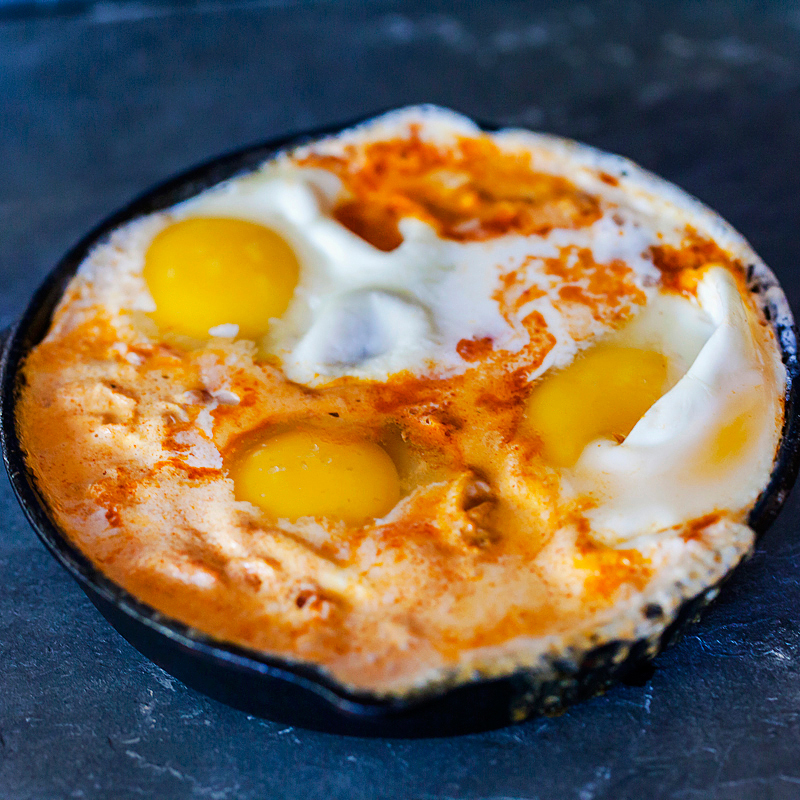 Mexican shakshuka recipe cast iron skillet with eggs simmering in a tomato crema sauce.